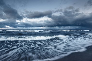 Kışın Baltık Denizi 'nin üzerindeki fırtına bulutları, uzun pozlama. Dramatik günbatımı gökyüzü, dalgalar ve su sıçramaları. Koyu deniz manzarası. Almanya