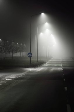 Gecenin karanlığında sisli, boş, aydınlık bir otoyol. Yol tabelası yakın plan. Karanlık şehir manzarası, şehir manzarası. Riga, Letonya. Tehlikeli sürüş, hız, özgürlük, konsept görüntü