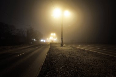 Gecenin karanlığında sisli, boş, aydınlık bir otoyol. Yol tabelası, fenerler yakın plan. Karanlık şehir manzarası, şehir manzarası. Riga, Letonya. Tehlikeli sürüş, konsept görüntü