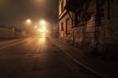 Geceleyin sisli, boş, aydınlık asfalt bir yol. Köprü arka planda. Riga, Letonya. Karanlık endüstriyel şehir