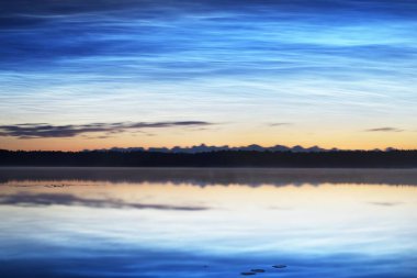 Yaz gündönümü gecesinde Saimaa Gölü 'nün üzerinde gece parlayan bulutlar ve sis vardı. Altın güneş ışığı. Uzun pozlama. Destansı bulut manzarası. Doğal desen. Suyun simetri yansımaları. Finlandiya