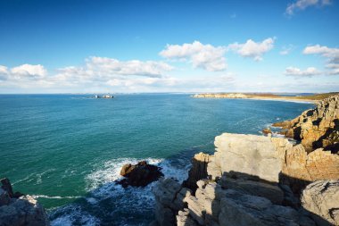 Pointe de Pen-Hir 'in kayalık sahili, uçurumlara yakın. Bulutlu mavi gökyüzü, masmavi su, fırtınalı dalgalar. Dramatik bulut manzarası. Crozon Yarımadası, Britanya, Fransa