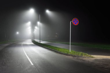 Gece sisli bir ortamda bomboş bir otoyol. Sokak lambaları ve yol işaretleri yakın. Karanlık şehir manzarası, şehir manzarası. Riga, Letonya. Tehlikeli sürüş, hız, özgürlük, konsept görüntü