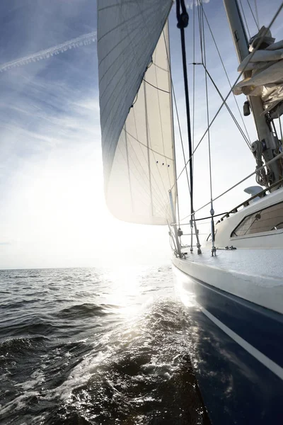 夏日阳光明媚 蓝色游艇在开阔的海面上航行 从甲板到船头和船帆的近景 浪花和水花四溅 晴朗的蓝天 有卷云和飞机轨道 — 图库照片