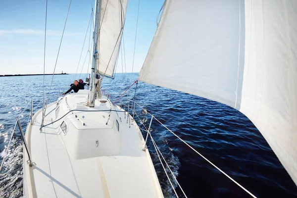 A couple of people on the white yacht sailing on a clear day. Top down view from the bow to the deck, mast and sails. Recreation and summer sport theme. Ruhnu island, Estonia