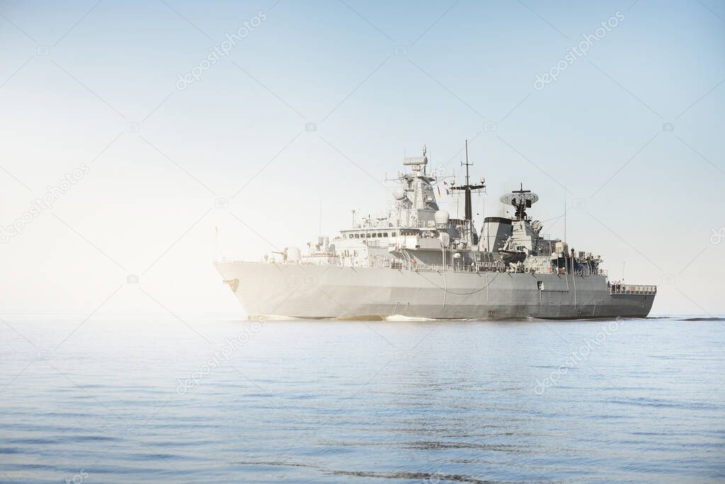 Large grey modern warship sailing in still water. Clear blue sky. Baltic sea, Germany. Global communications, international security theme