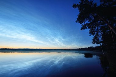 Yaz gündönümü gecesinde Saimaa Gölü 'nün üzerinde gece parlayan bulutlar ve sis vardı. Altın güneş ışığı. Uzun pozlama. Destansı bulut manzarası. Doğal desen. Suyun simetri yansımaları. Finlandiya