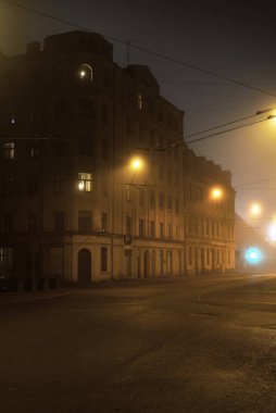 Geceleyin sisli bir şekilde eski tarihi binaların ve evlerin arasından aydınlatılmış boş bir asfalt yol. Sokak lambaları (fenerler) yakın plan. Riga, Letonya. Karanlık şehir manzarası