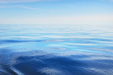 Deniz suyu dokusu. Açık mavi gökyüzü, beyaz bulutlar ve uçak izleri. Sudaki yansımalar. Baltık Denizi, Estonya