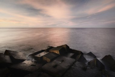 Renkli günbatımı gökyüzüne karşı dalgalı su. Göz kamaştırıcı deniz manzarası. Mavi bulutların arasından geçen altın gün batımı ışığı. Uzun pozlama. Baltık Denizi, Riga Körfezi, Letonya