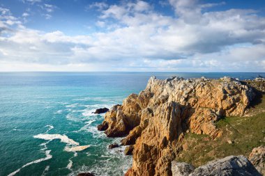 Pointe de Pen-Hir 'in kayalık sahili, uçurumlara yakın. Bulutlu mavi gökyüzü, masmavi su, fırtınalı dalgalar. Dramatik bulut manzarası. Crozon Yarımadası, Britanya, Fransa