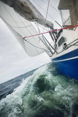 Yağmurlu bir günde, fırtınalı bir havada yat gezintisi. Güverteden pruvaya, direğe ve yelkenlere yakın görüntü. Dramatik fırtınalı gökyüzü, kara bulutlar. Dalgalar ve su sıçramaları. Kötü hava. Baltık Denizi, İsveç