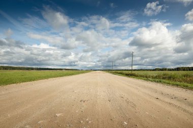 Yağmurdan sonra tarlalardan geçen boş bir köy yolu. Dramatik gökyüzü, destansı bulutlar. Hava kararsız. Transformatör direkleri yakın çekim. Letonya