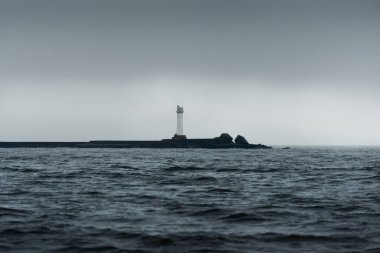 Fırtınadan sonra kara bulutların altında bir deniz feneri. Yelkenli teknenin manzarası. Dramatik fırtınalı gökyüzü. Kuzey denizi, Norveç. Atmosferik manzara. Umut ve barışın sembolü