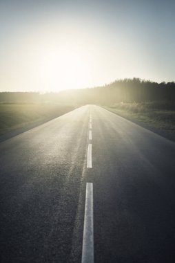 Sıcak bir yaz gününde gün batımında boş bir otoyol. Arka planda orman var. Kırsal alanlarda araba sürmek. Boş zaman aktivitesi, eğlence teması. Letonya