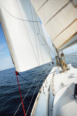 Güneşli bir yaz gününde beyaz bir yat denize açılıyor. Güverteden pruvaya, direğe ve yelkenlere yakın görüntü. Dalgalar ve su sıçramaları. Açık mavi gökyüzü. Finlandiya Körfezi