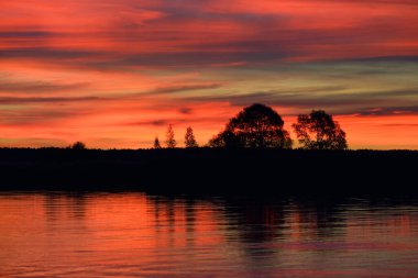 Sonbaharda göl ve ormanın üzerinde destansı kızıl günbatımı gökyüzü. Dramatik bulut manzarası. Sudaki simetri yansımaları, doğal ayna. Idyllic kırsal kesim. Gauja Ulusal Parkı, Sigulda, Letonya