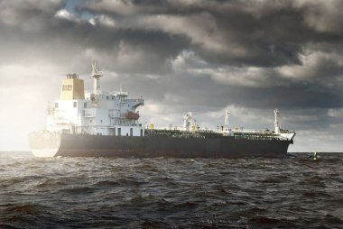 Büyük bir kargo gemisi dramatik fırtınalı gökyüzünün altında açık denizde yelken açıyor. Destansı deniz manzarası. Nakliye, küresel iletişim, teslimat, yakıt ve güç üretimi, endüstri, lojistik