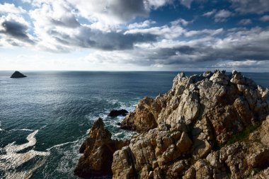 Pointe de Pen-Hir 'in kayalık sahili, uçurumlara yakın. Bulutlu mavi gökyüzü, masmavi su, fırtınalı dalgalar. Dramatik bulut manzarası. Crozon Yarımadası, Britanya, Fransa