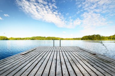 Nehrin yakınındaki ahşap iskele. Arka planda Evergreen kozalaklı orman var. Açık mavi gökyüzü, suda yansımalar. Idyllic yaz manzarası. Eko turizm, eğlence teması. Finlandiya