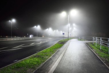 Gece sisli bir havada karayolu yakınında boş bir bisiklet yolu. Fenerler yakın plan. Ulaşım, tehlikeli sürüş, eğlence ve sağlıklı yaşam tarzı teması. Riga, Letonya
