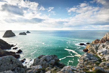 Pointe de Pen-Hir 'in kayalık sahili, uçurumlara yakın. Bulutlu mavi gökyüzü, masmavi su, fırtınalı dalgalar. Dramatik bulut manzarası. Crozon Yarımadası, Britanya, Fransa