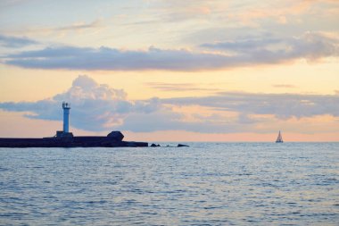 Baltık deniz kıyısında günbatımının destansı gökyüzü, deniz feneri yakın çekim. Parlayan altın bulutlar, sıcak güneş ışığı. Dramatik bulut manzarası. Letonya