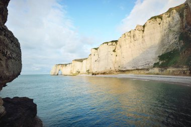 Etretat 'ın beyaz kayalıklarının manzarası panoramik alçak açılı. Açık mavi gökyüzü, gök mavisi su. Fransa, Normandiya 'da yaz tatili. Seyahat yeri, ulusal dönüm noktası, manzara, tarih.