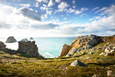 Pointe de Pen-Hir 'in kayalık sahili, uçurumlara yakın. Bulutlu mavi gökyüzü, masmavi su, fırtınalı dalgalar. Dramatik bulut manzarası. Crozon Yarımadası, Britanya, Fransa