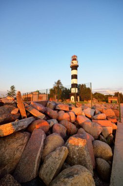 Riga körfezinin kayalık sahilinde eski bir siyah beyaz deniz feneri, yakın plan. Baltık Denizi, Letonya. Açık günbatımı gökyüzü. Görüntü kavramı, barış ve umut sembolü, yön bulma, seyahat hedefi
