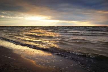 Dramatik günbatımı bulutları altında fırtınalı Baltık Denizi. Kumlu sahilden bir manzara. Riga Körfezi, Letonya. Destansı deniz manzarası. Karanlık sonbahar sahnesi. Meteoroloji, ekoloji, çevre koruma, iklim değişikliği