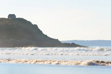 Uçurumun kenarındaki yalnız geleneksel ev Douarnenez körfezinin kumlu kıyılarından bir manzara. Açık mavi gökyüzü. Dalgalar ve su sıçramaları. Brittany, Fransa. Seyahat yerleri, gezi teması