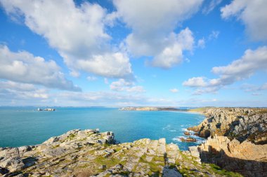 Pointe de Pen-Hir 'in kayalık sahili, uçurumlara yakın. Bulutlu mavi gökyüzü, masmavi su, fırtınalı dalgalar. Dramatik bulut manzarası. Crozon Yarımadası, Britanya, Fransa