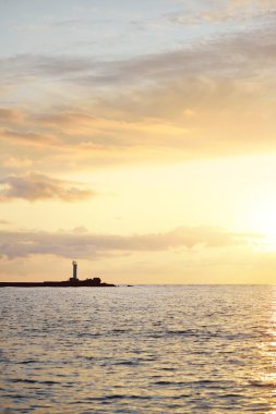 Baltık deniz kıyısında günbatımının destansı gökyüzü, deniz feneri yakın çekim. Parlayan altın bulutlar, sıcak güneş ışığı. Dramatik bulut manzarası. Letonya