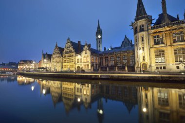 St. Michael köprüsü yakınlarındaki aydınlanmış gezinti güvertesi ve Gent şehrinin tarihi merkezindeki St. Bavo Katedrali. Gece manzarası. Suyun simetri yansımaları. Seyahat rehberi, gezi teması. Belçika