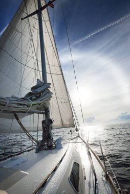 Güneşli bir yaz gününde açık denizde yelken açan beyaz bir yat. Güverteden pruva ve yelkenlere kadar yakın çekim. Dalgalar ve su sıçramaları. Sirus bulutları ve uçak izleri olan açık mavi bir gökyüzü. Hollanda