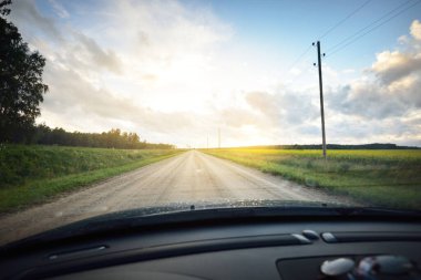 Yağmurdan sonra tarlalardan geçen boş bir köy yolu. Dramatik gökyüzü, destansı bulutlar. Arabadan bir manzara. Hava kararsız. - Letonya. Kasırga, fırtına, meteoroloji, ekoloji, doğal olaylar