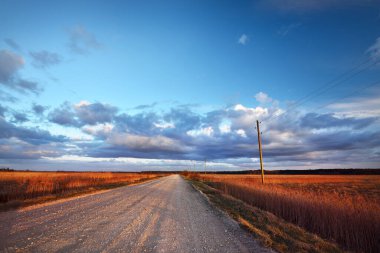 Yağmurdan sonra tarlalardan geçen boş bir köy yolu. Dramatik mavi gökyüzü. Sonbaharda kararsız hava. - Letonya. Kasırga, fırtına, meteoroloji, ekoloji, iklim değişikliği
