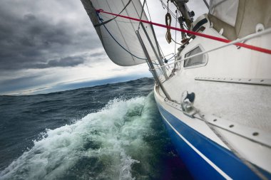 Yağmurlu bir günde, fırtınalı bir havada yat gezintisi. Güverteden pruvaya, direğe ve yelkenlere yakın görüntü. Dramatik fırtınalı gökyüzü, kara bulutlar. Dalgalar ve su sıçramaları. Kötü hava. Baltık Denizi, İsveç