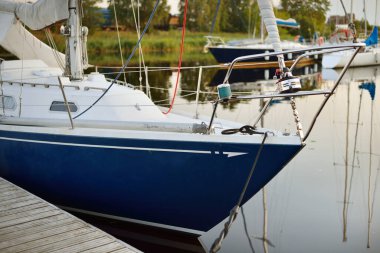 Zarif ve modern yelkenli tekneler (kiralık) açık bir günde yat limanındaki bir rıhtıma demirlediler. Ulaşım, spor ve eğlence teması. İsveç. Mavi yelkenli donanımlı yelkenli. Yakın plan.