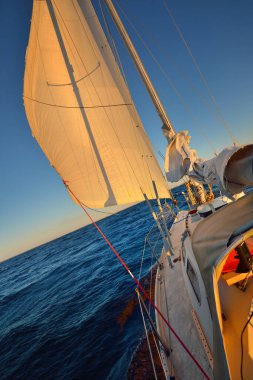 Gün batımında fırtınadan sonra açık bir Baltık denizinde yat gezintisi. Güverteden pruvaya, direğe ve yelkenlere yakın görüntü. Açık mavi gökyüzü. Dalgalar ve su sıçramaları. İsveç