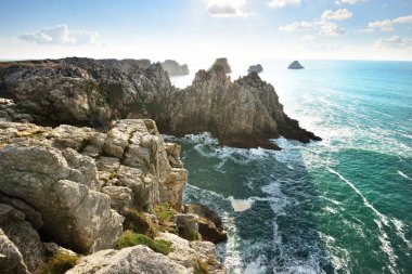 Pointe de Pen-Hir 'in kayalık sahili, uçurumlara yakın. Bulutlu mavi gökyüzü, masmavi su, fırtınalı dalgalar. Dramatik bulut manzarası. Crozon Yarımadası, Britanya, Fransa