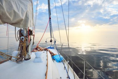 Gün batımında durgun suda yüzen beyaz bir yat. Güverteden pruvaya, direğe ve yelkenlere bir manzara. Şaşırtıcı bulut manzarası. Doğal ayna. Spor ve eğlence teması. Baltık Denizi, İsveç