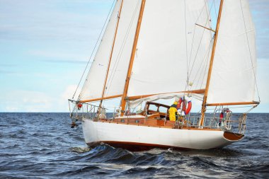 Eski, pahalı, ahşap bir yelkenli (yawl) yakın çekim, açık denizde yelken. Dramatik bulut manzarası. Maine sahili, ABD