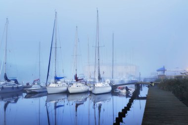 Yelkenli tekneler, güneşin doğuşunda yoğun beyaz bir sisle bir rıhtıma demirlediler. Kiel, Almanya 'daki yat kulübü. Spor, eğlence, ulaşım teması