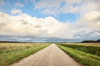 Yağmurdan sonra tarlalardan geçen boş bir köy yolu. Dramatik gökyüzü, destansı bulutlar. Hava kararsız. - Letonya. Kasırga, fırtına, meteoroloji, ekoloji, iklim değişikliği, doğal olaylar