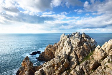 Pointe de Pen-Hir 'in kayalık sahili, uçurumlara yakın. Bulutlu mavi gökyüzü, masmavi su, fırtınalı dalgalar. Dramatik bulut manzarası. Crozon Yarımadası, Britanya, Fransa