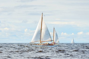 Eski, pahalı, ahşap bir yelkenli (yawl) yakın çekim, açık denizde yelken. Dramatik bulut manzarası. Maine sahili, ABD