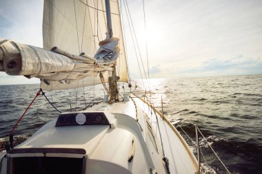 Güneşli bir yaz gününde açık denizde yelken açan beyaz bir yat. Güverteden pruva ve yelkenlere kadar yukarıdan aşağıya doğru. Dalgalar ve su sıçramaları. Sirus bulutları ve uçak izleri olan açık mavi bir gökyüzü. Hollanda