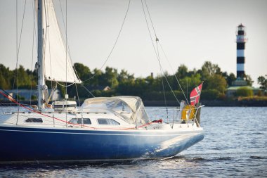 Gün batımında Riga körfezinde mavi yelkenli yelkenli yelkenli. Yakın plan. Baltık Denizi, Letonya. Arka planda deniz feneri var. Yarış, spor, eğlence, eğlence aktivitesi, takım çalışması kavramları.